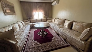 A living room with a large L-shaped sofa, a round coffee table, and a patterned rug. - Accommodation 20 minutes from Marrakech (Chwiter)