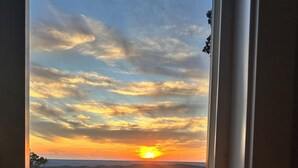 Ein Sonnenuntergang durch ein Fenster, mit blauem Himmel und fernen Hügeln.