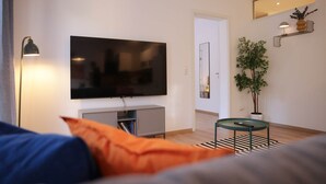 A modern living room with a flat-screen TV mounted on the wall, a small side table, a potted plant, and a striped rug.