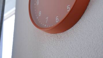Eine runde, orangefarbene Wanduhr mit weißen Zahlen und Zeigern, an einer strukturierten Wand befestigt.
