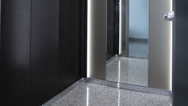 A modern elevator with a glass door, a polished granite floor, and a dark wall.