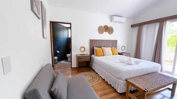 Een slaapkamer met een bed, een nachtkastje, een bankje, een sofa en een deur naar een andere kamer.