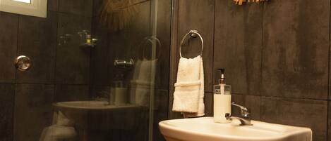 A bathroom with a glass-enclosed shower, a white pedestal sink, a mirror with a sunburst frame, and dark wooden walls.