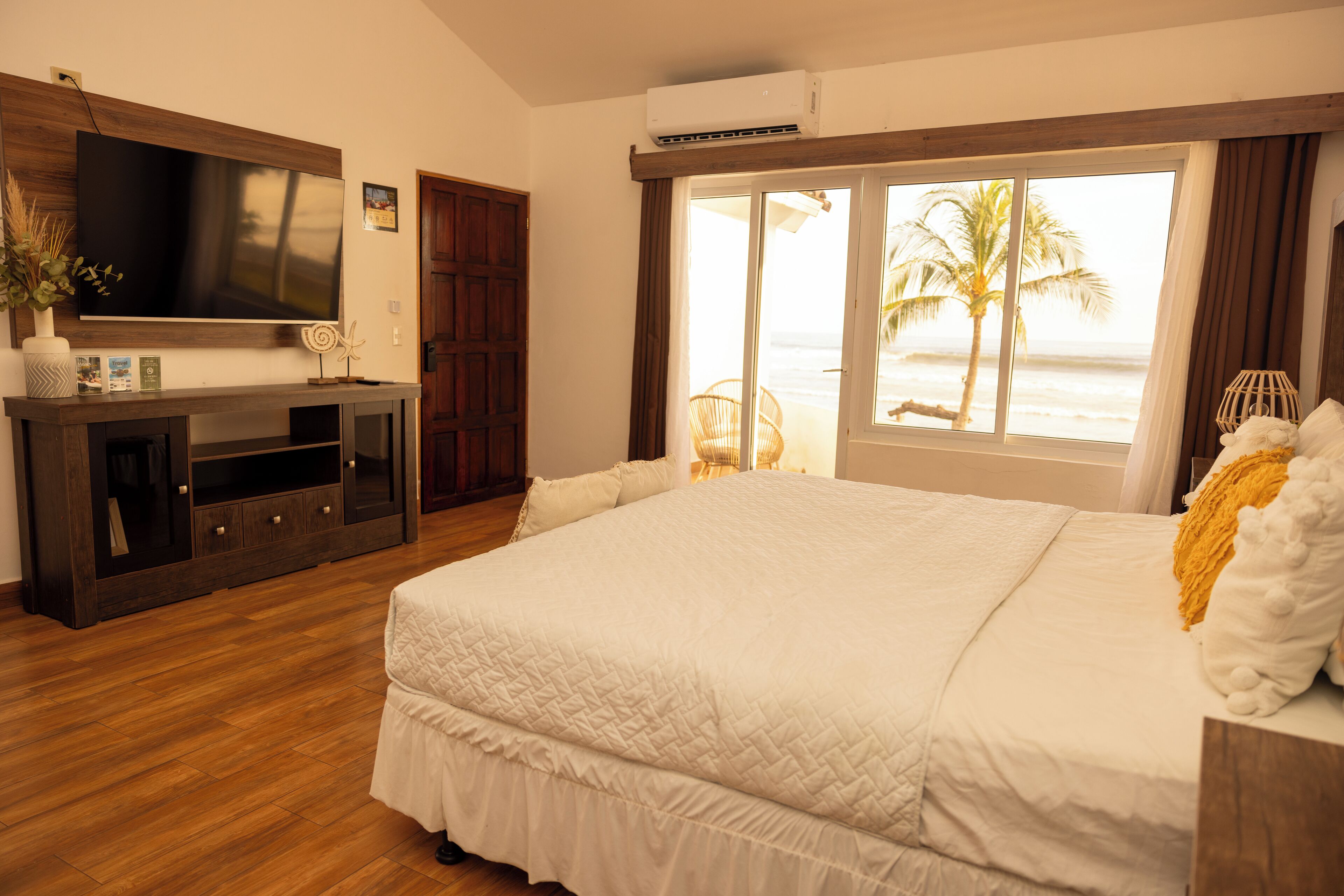 Une chambre d’hôtel avec un grand lit, une télévision, un plancher en bois et une fenêtre donnant sur la plage.