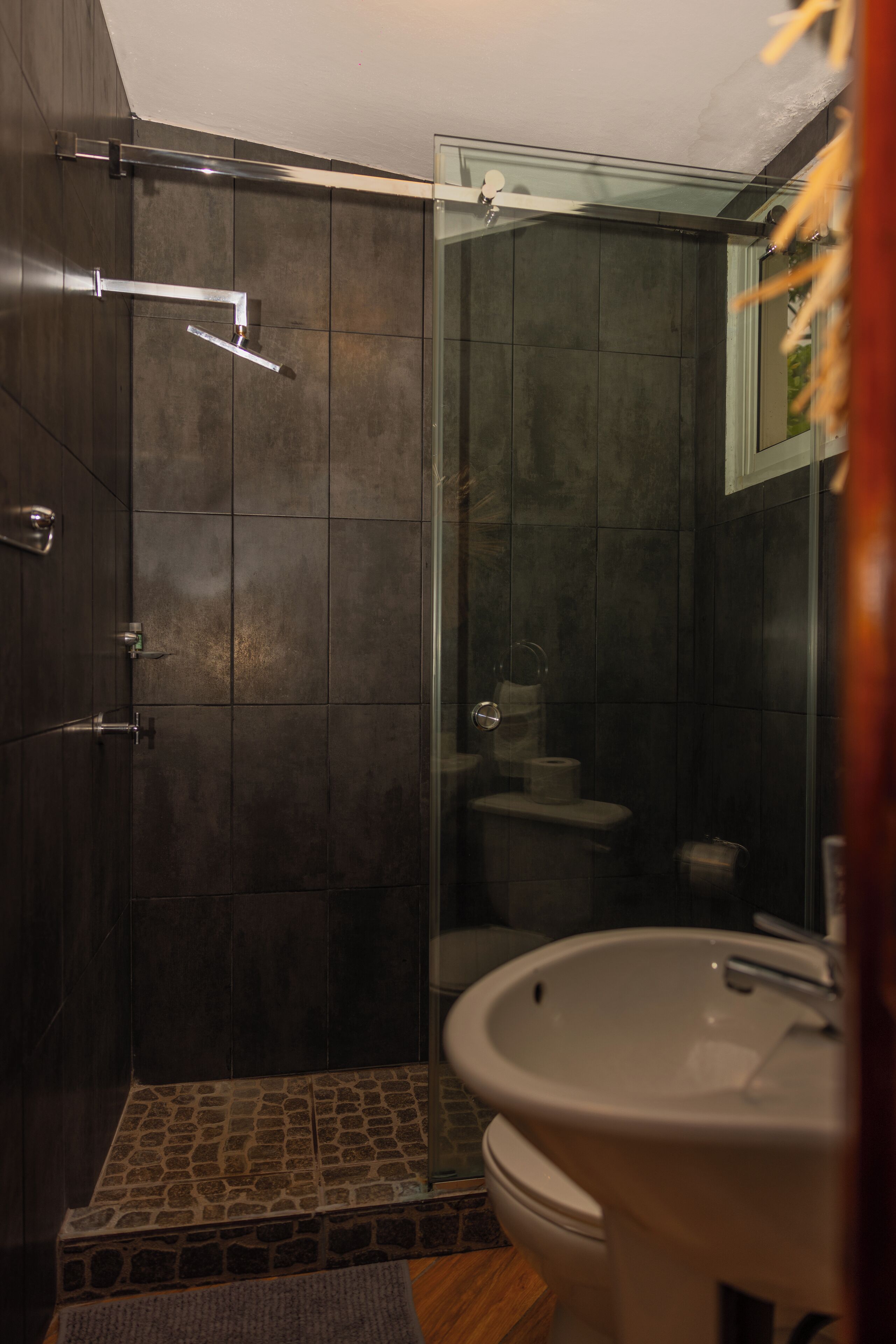 Een badkamer met een douche met glazen wand, een witte wastafel en een toilet.
