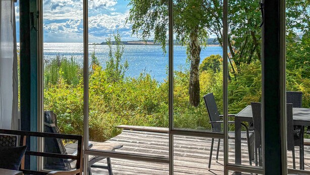 A room with a large window overlooking a body of water and greenery.