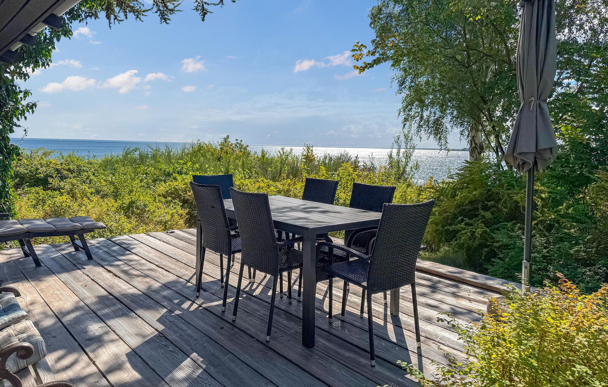 Terraza de madera con mesa y sillas, con vista a un cuerpo de agua.