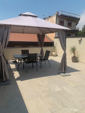 En udendørs terrasse med et bord og stole under en stor parasol.