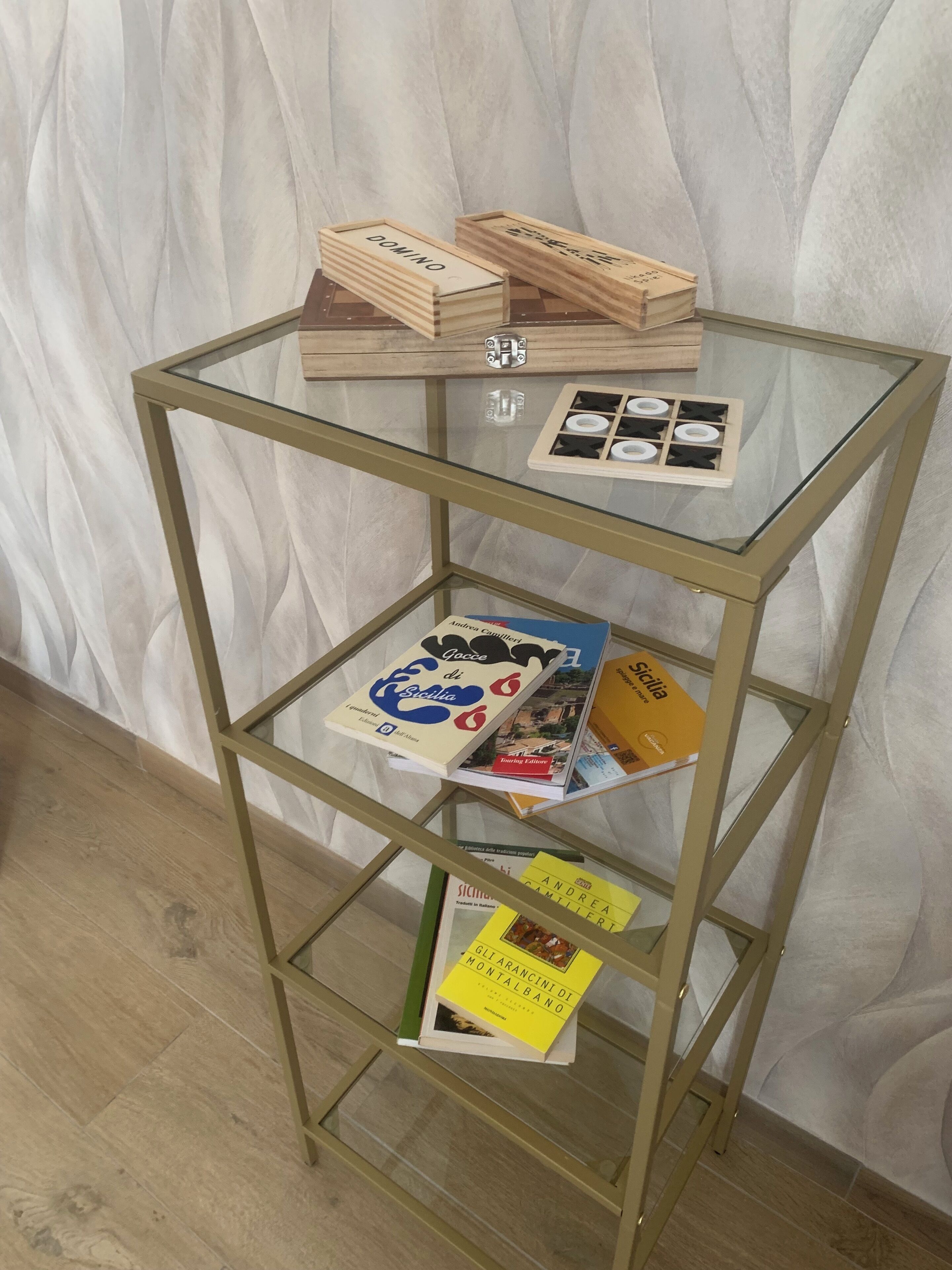 Una estantería metálica con tapa de cristal, libros y un juego de mesa.