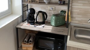 A kitchen with a coffee maker, kettle, toaster, and a microwave. There are potted plants on the shelves, and a sign about Sicilian cuisine. - Etna Guest House (Belpasso)