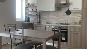 A modern kitchen with light wood cabinetry, a central island, and a dining area with a wooden table and chairs. - Etna Guest House (Belpasso)