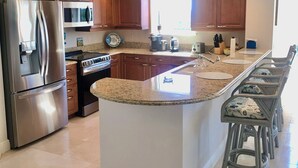 A modern kitchen with a central island, stainless steel appliances, wooden cabinets, and a large window providing natural light.