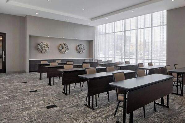 A conference room with multiple tables and chairs, large windows, and decorative wall art. - AC Hotel Auburn (Auburn)