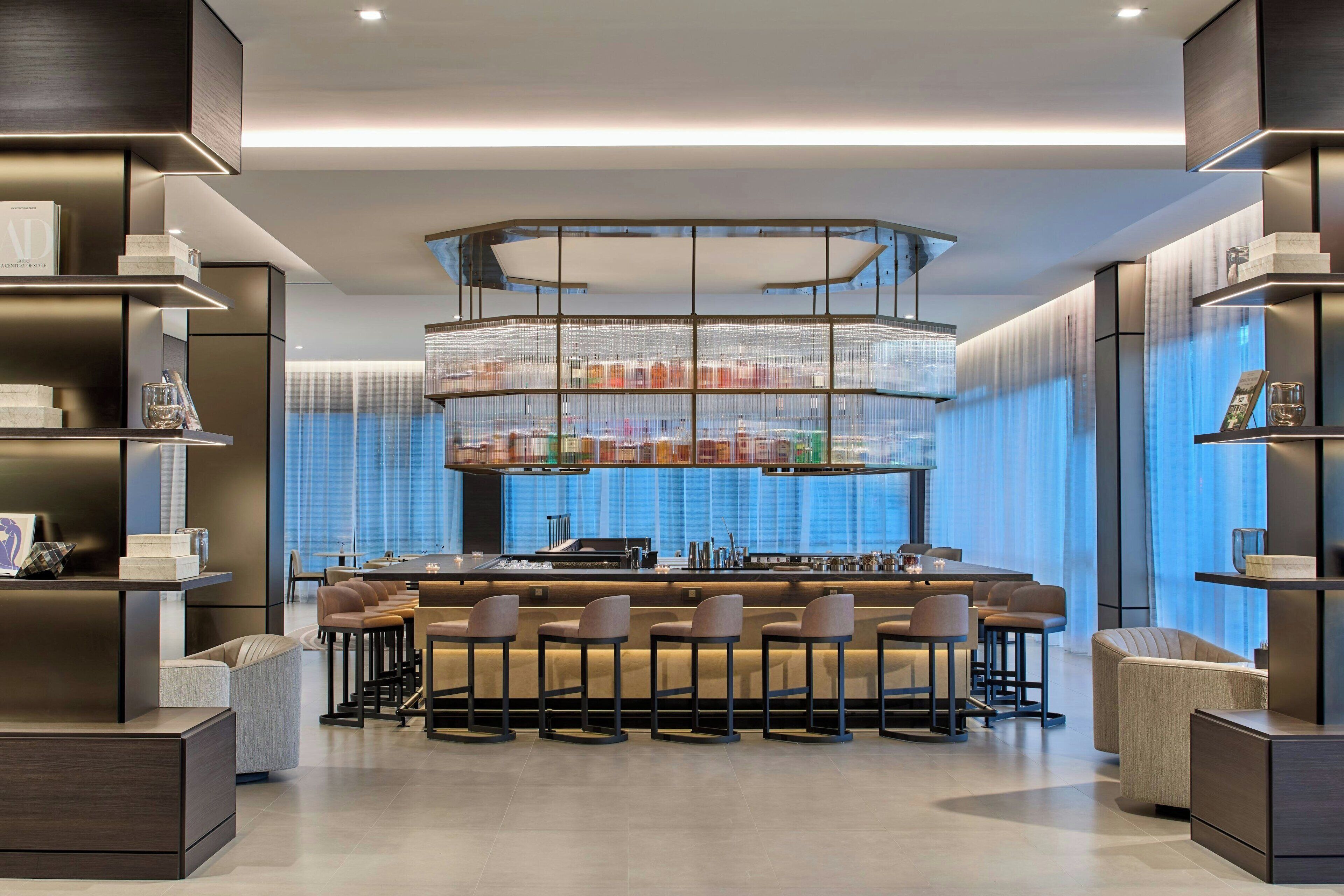 A modern bar area with a central island, bar stools, and a tiered shelving unit displaying various items.
