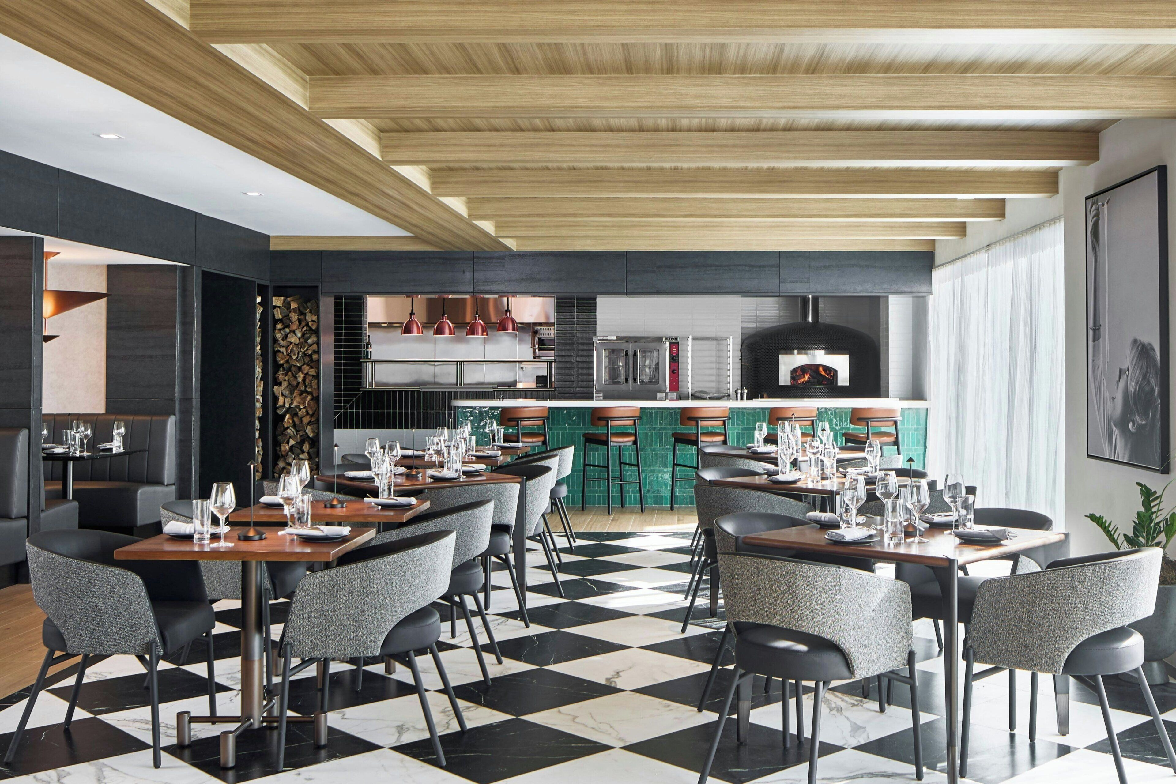 Un restaurante moderno con suelo a cuadros, vigas de madera en el techo y una zona de cocina central.