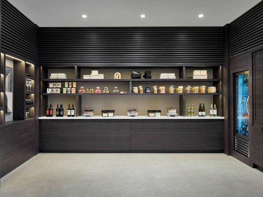 A modern kitchen with dark wood cabinetry, a central island with a white countertop, and various kitchen appliances and storage containers.