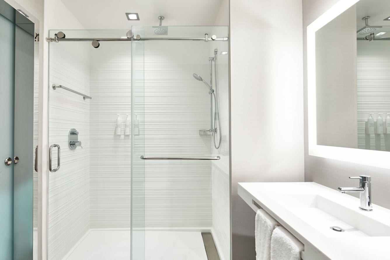 Un baño moderno con ducha envuelta en vidrio, un lavabo blanco y un espejo grande.