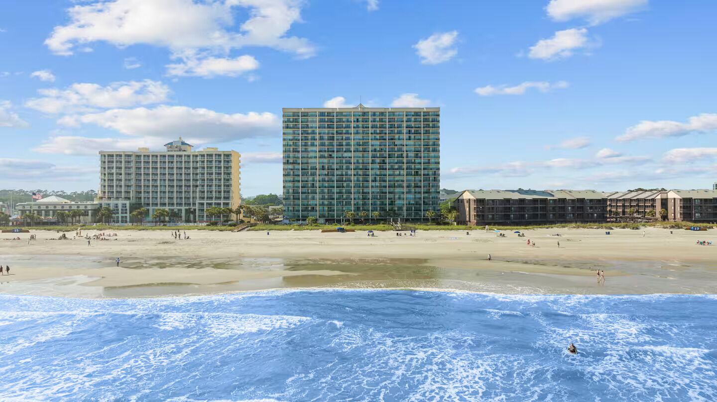 Ein Strandhotel mit mehreren Hochhäusern, Sandstrand und Meereswellen.