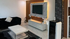 A modern living room with a flat-screen TV mounted on a marble wall, a white console table, a black sofa, and a small black heater. - L'échapée belle (Beinheim)