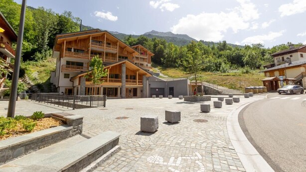 A modern hotel with a wooden facade, multiple balconies, and a paved courtyard.