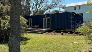 Una casa de contenedores azules con una puerta corredera de vidrio, un pequeño porche y un patio con césped.