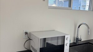 Una cocina con microondas, un lavamanos y una ventana con vistas a edificios.