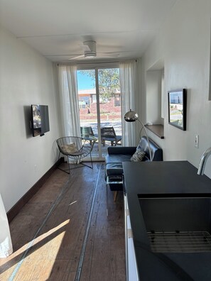 A modern living room with a flat-screen TV, a sofa, a chair, and a dining area with a table and chairs.