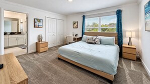 Een slaapkamer met een bed, nachtkastjes, een bureau, een stoel, een kledingkast en een raam met gordijnen.
