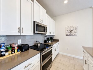 A modern kitchen with white cabinets, a microwave, a kettle, a toaster, and a blender on the countertop. - Luxury Pool Home Near Disney Resort Access (Kissimmee)