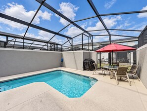 Une piscine extérieure couverte, agrémentée d’un parasol rouge, d’un barbecue et de mobilier de jardin.