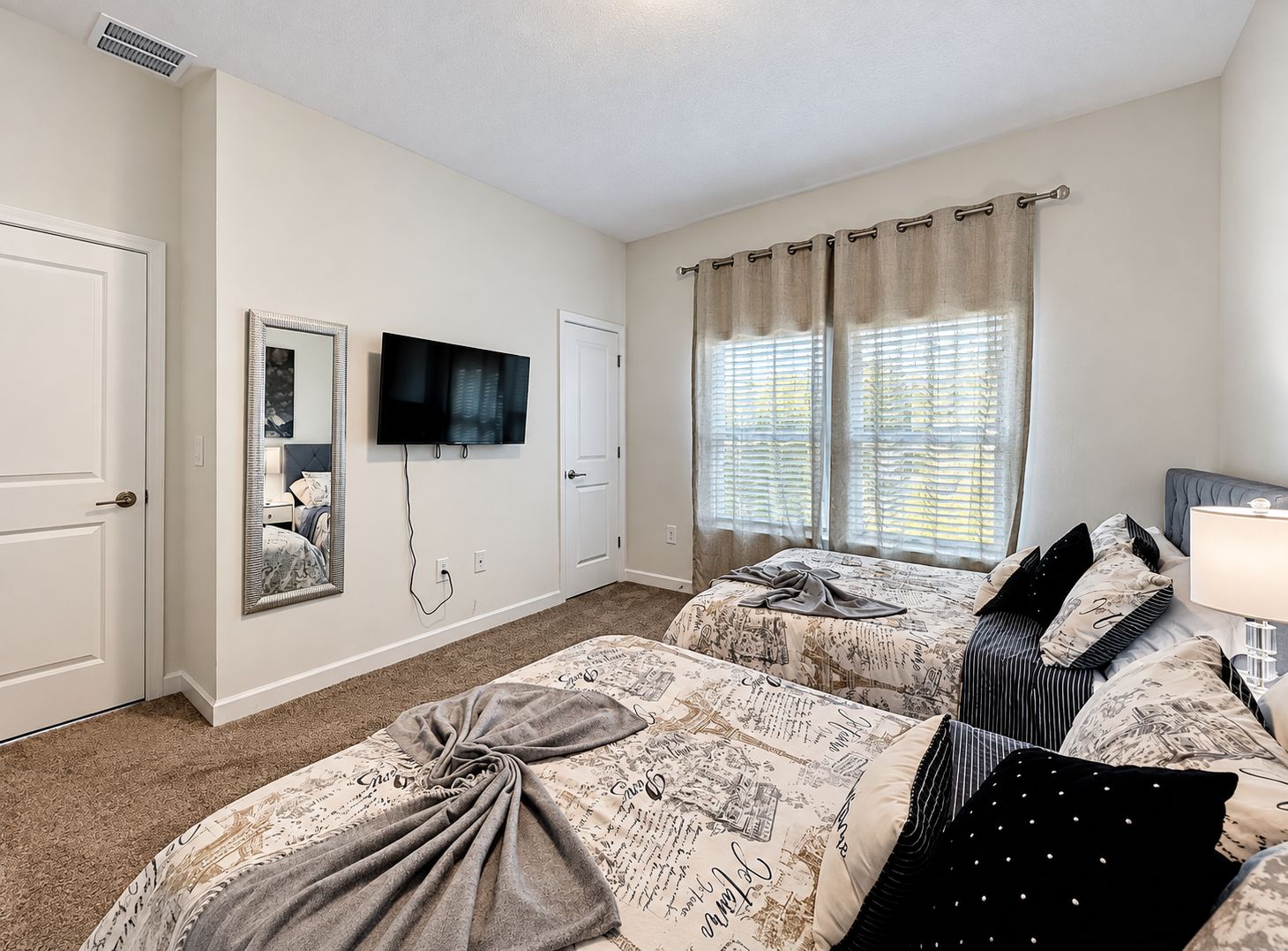 A hotel room with two beds, a television, a mirror, and a window with curtains.