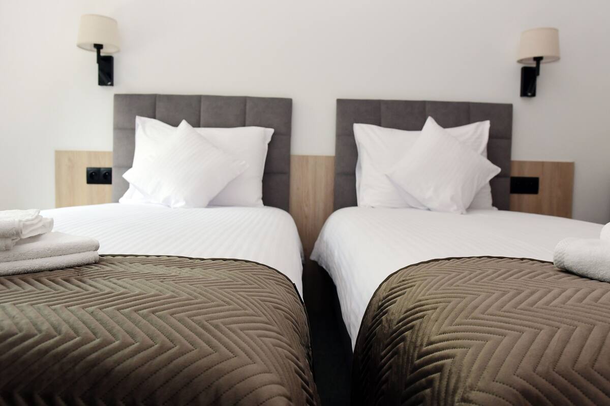 Two twin beds with grey headboards, white bedding, and a brown quilted bedspread.