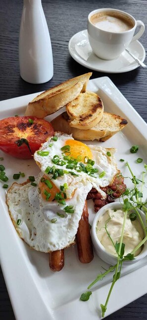 Un plato de desayuno con huevos, tocino, tostadas y una taza de café sobre una mesa.