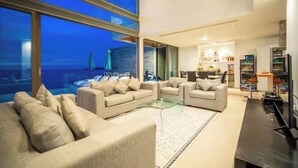 A modern living room with a glass coffee table, beige sofas, and a view of the ocean.