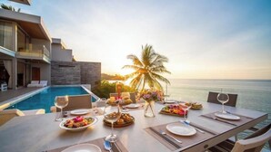 A dining table set for a meal with a view of the ocean and a palm tree.