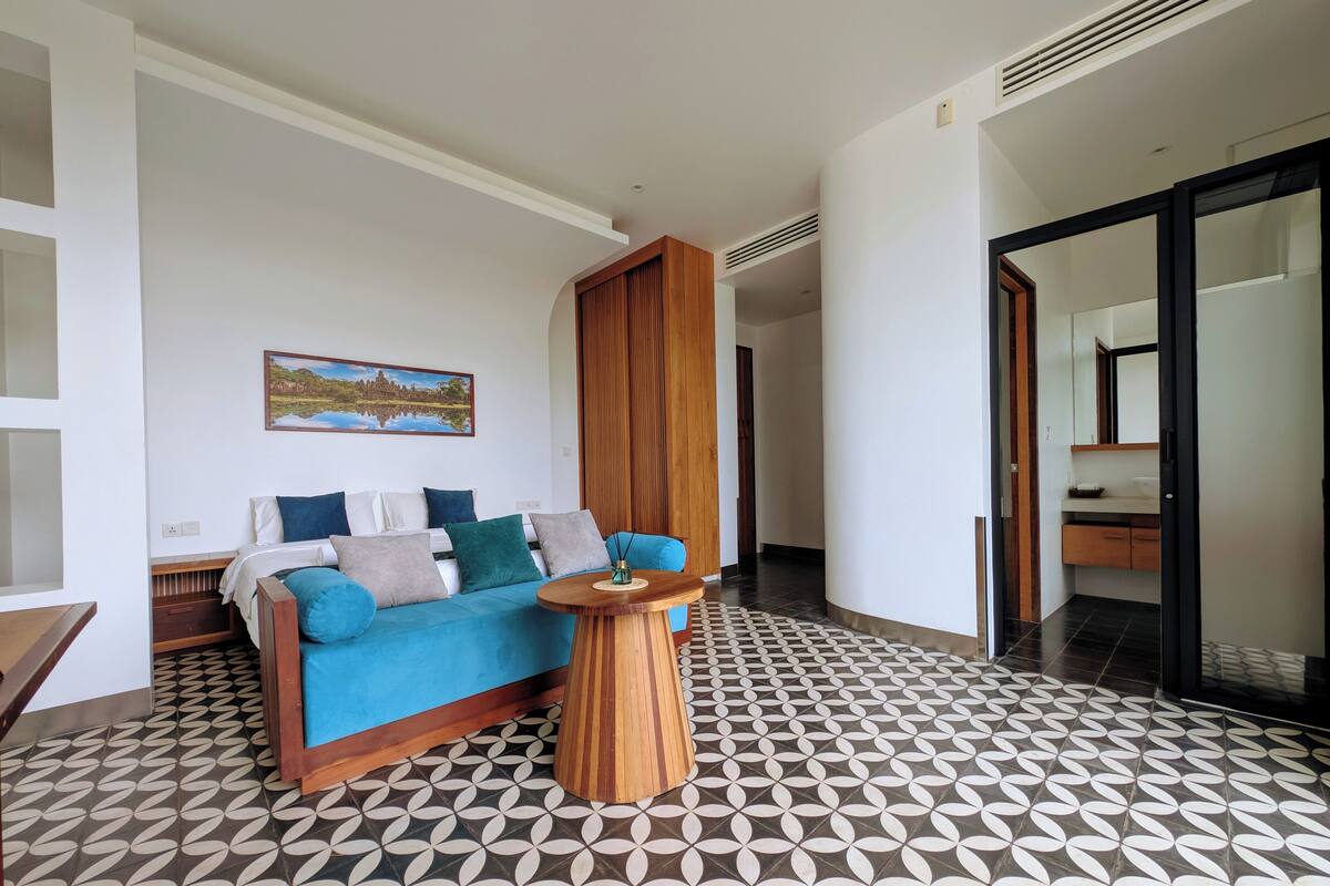 A modern living room with a blue sofa, a wooden coffee table, and patterned floor tiles.