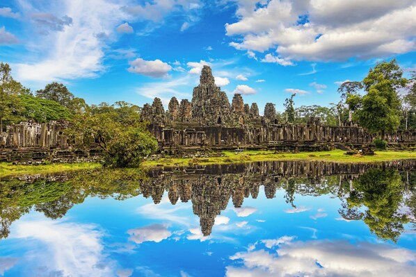 A historic temple complex with a reflection in the water, surrounded by lush greenery.