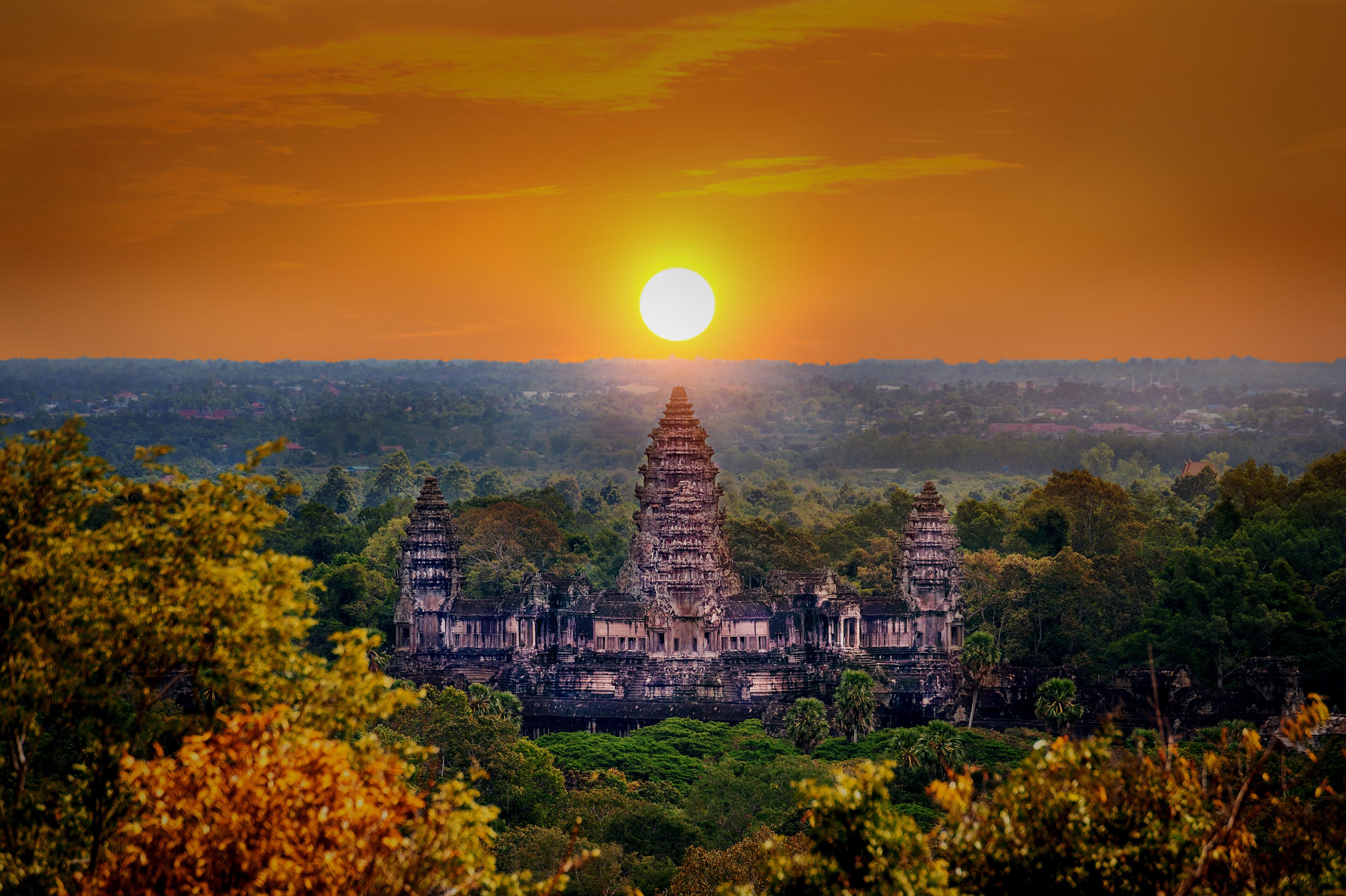 A temple complex with multiple towers, surrounded by dense greenery, under a sunset sky.