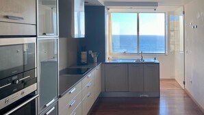 A modern kitchen with a built-in oven, a sink, and a window overlooking the sea. - Luxury Apartment on Lavadores Beach (Vila Nova de Gaia)
