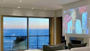 A modern living room with a large TV screen, white sofas, a wooden floor, and a view of the ocean. - Luxury Apartment on Lavadores Beach (Vila Nova de Gaia)