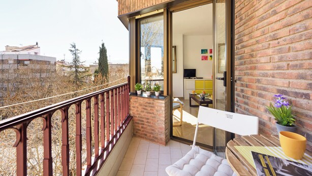 A balcony with a view of a cityscape, a brick wall, and a glass door leading to a room with a sofa and a table. - Beautiful Views, Balcony, Downtown (Granada)