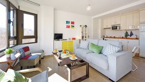 A modern living room with a sofa, coffee table, and a TV. There is a kitchen area with cabinets and a microwave. - Beautiful Views, Balcony, Downtown (Granada)