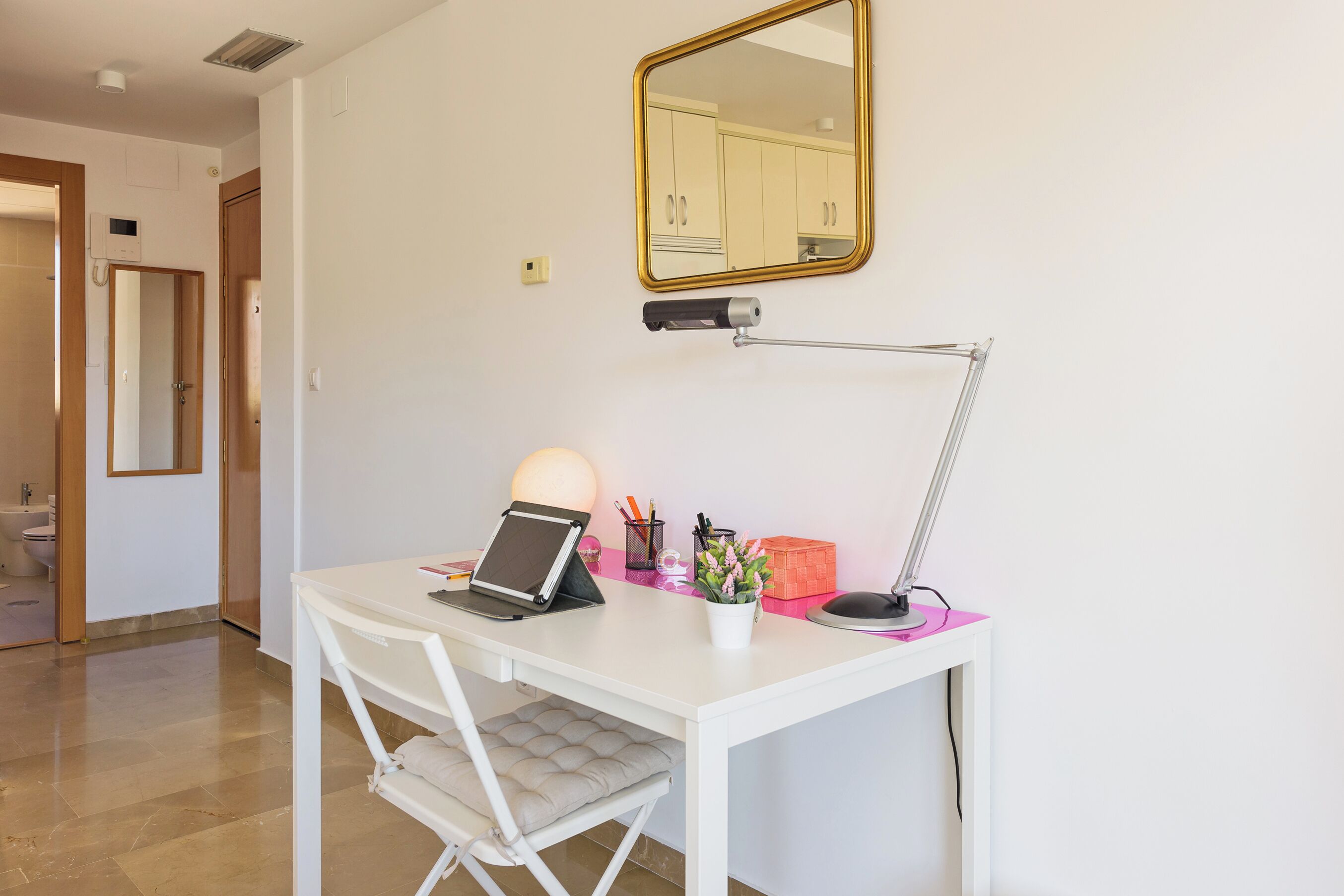 Un bureau blanc avec un ordinateur portable, une lampe de bureau et une petite plante en pot.