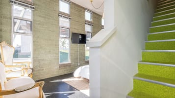 Een moderne hotelkamer met een groot raam, een flatscreen televisie, een witte badkuip en een trap met groene treden.