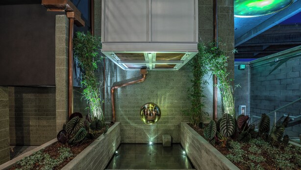 Un espace intérieur moderne, doté d’une sculpture centrale réfléchissante, entouré de jardinières et d’un mur de briques.