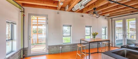A spacious kitchen with a wooden ceiling, large windows, and a bright orange floor.