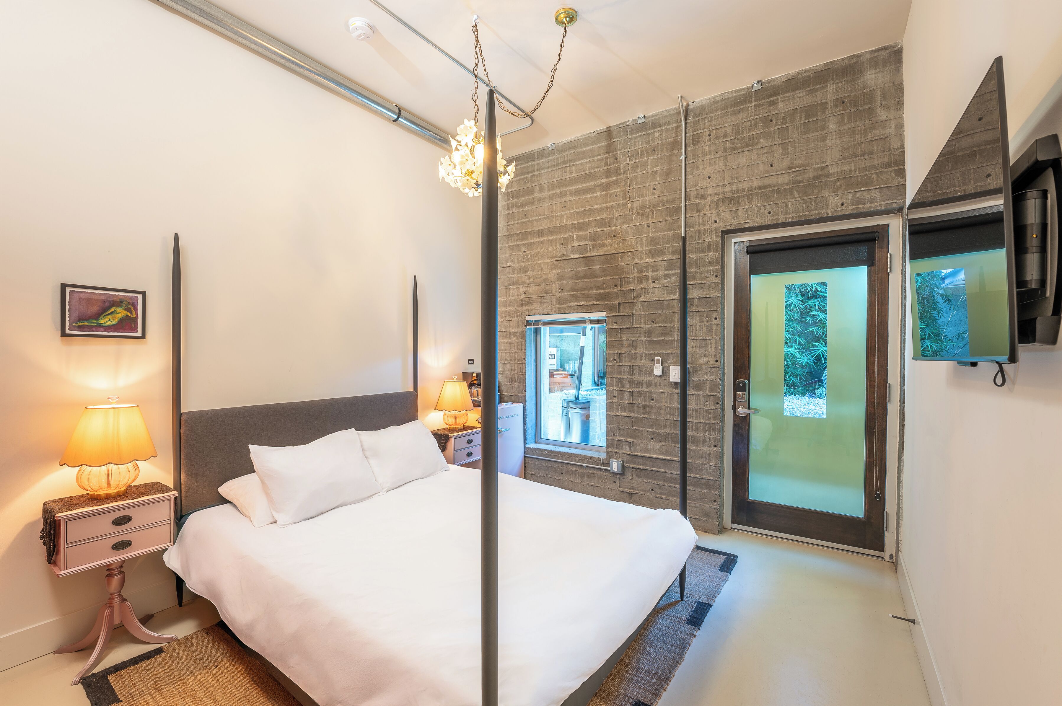 A modern bedroom with a large bed, bedside lamps, a wooden accent wall, a sliding glass door, and a mounted TV.
