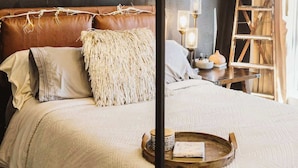 Une chambre à coucher avec un lit à baldaquin, un luminaire suspendu, une table de chevet avec une lampe et une échelle en bois appuyée contre le mur.