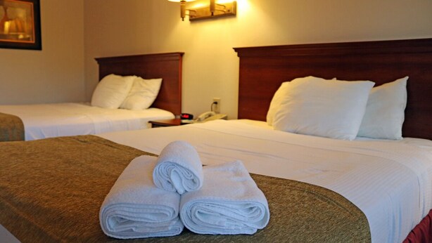 A hotel room with two beds, each with wooden headboards and white bedding. There are rolled white towels on a brown headboard. - Vision Inn Motel (Falls City)