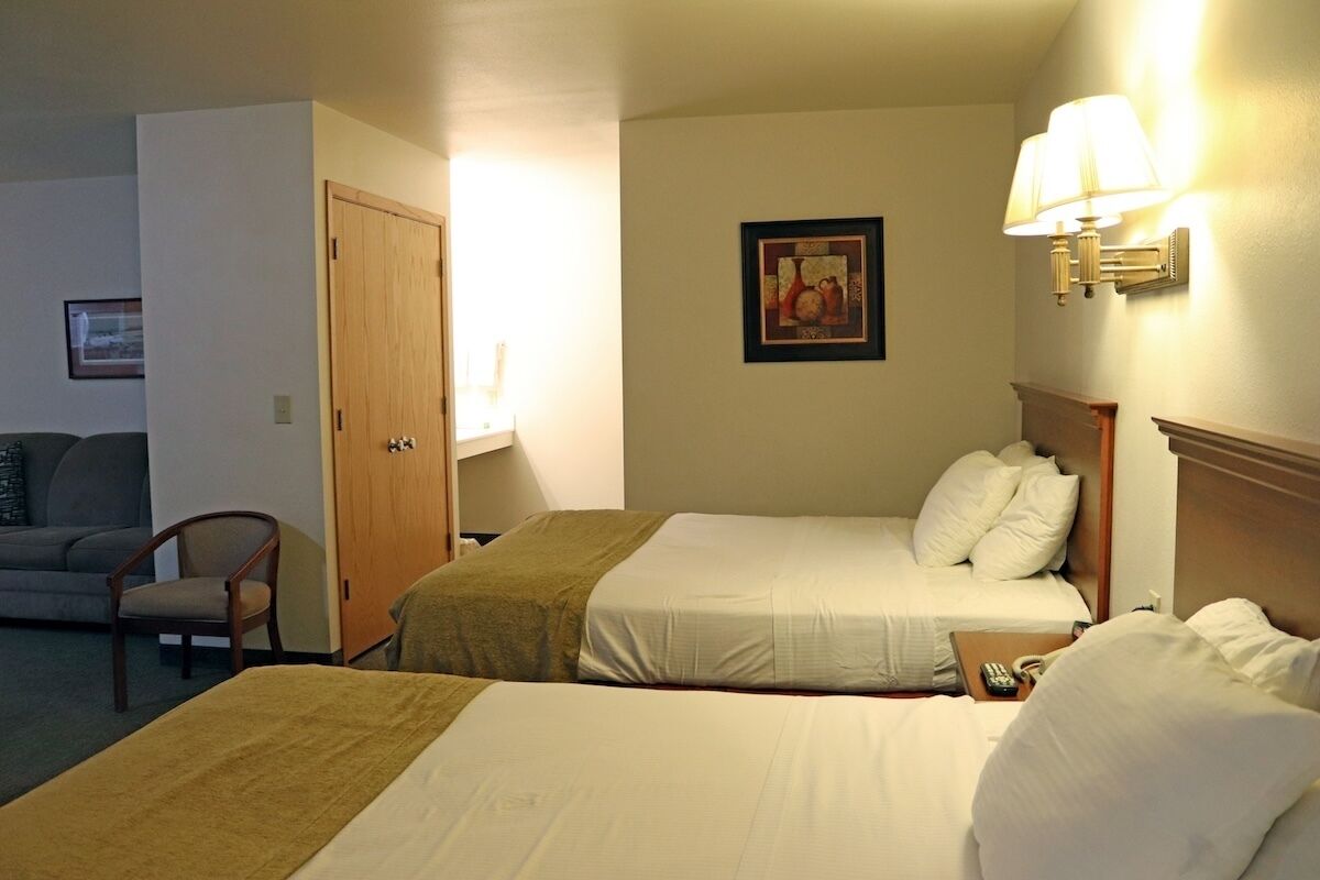Quarto de hotel com duas camas, um sofá, uma cadeira e um quadro na parede.